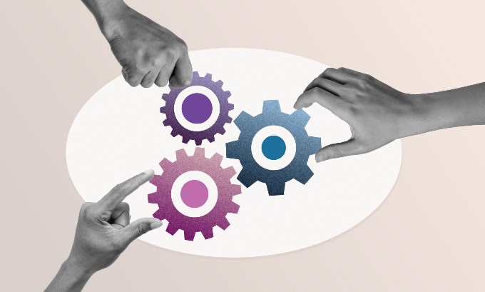 Three hands place three different sized gears close together.