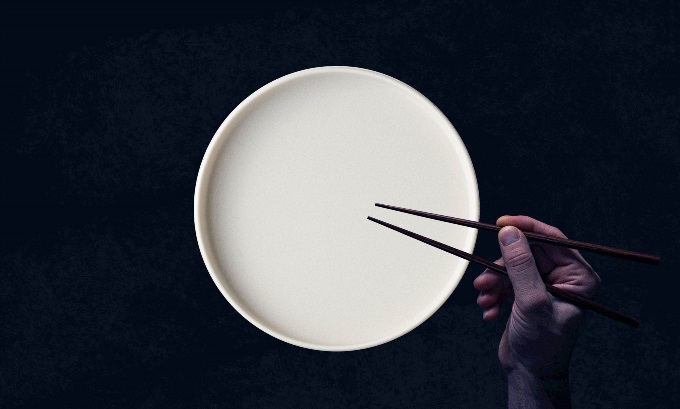 A white, empty plate with a waiting hand holding chopsticks.