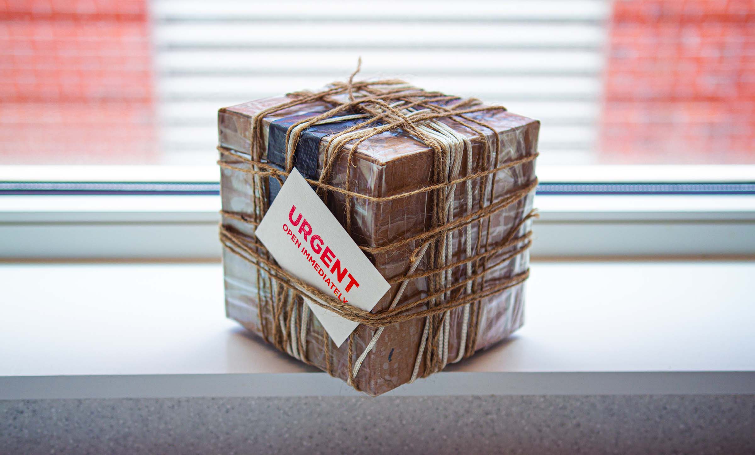 A difficult-to-open box haphazardly tied in twine and covered in tape. A note on the box says, "Urgent. Open Immediately."