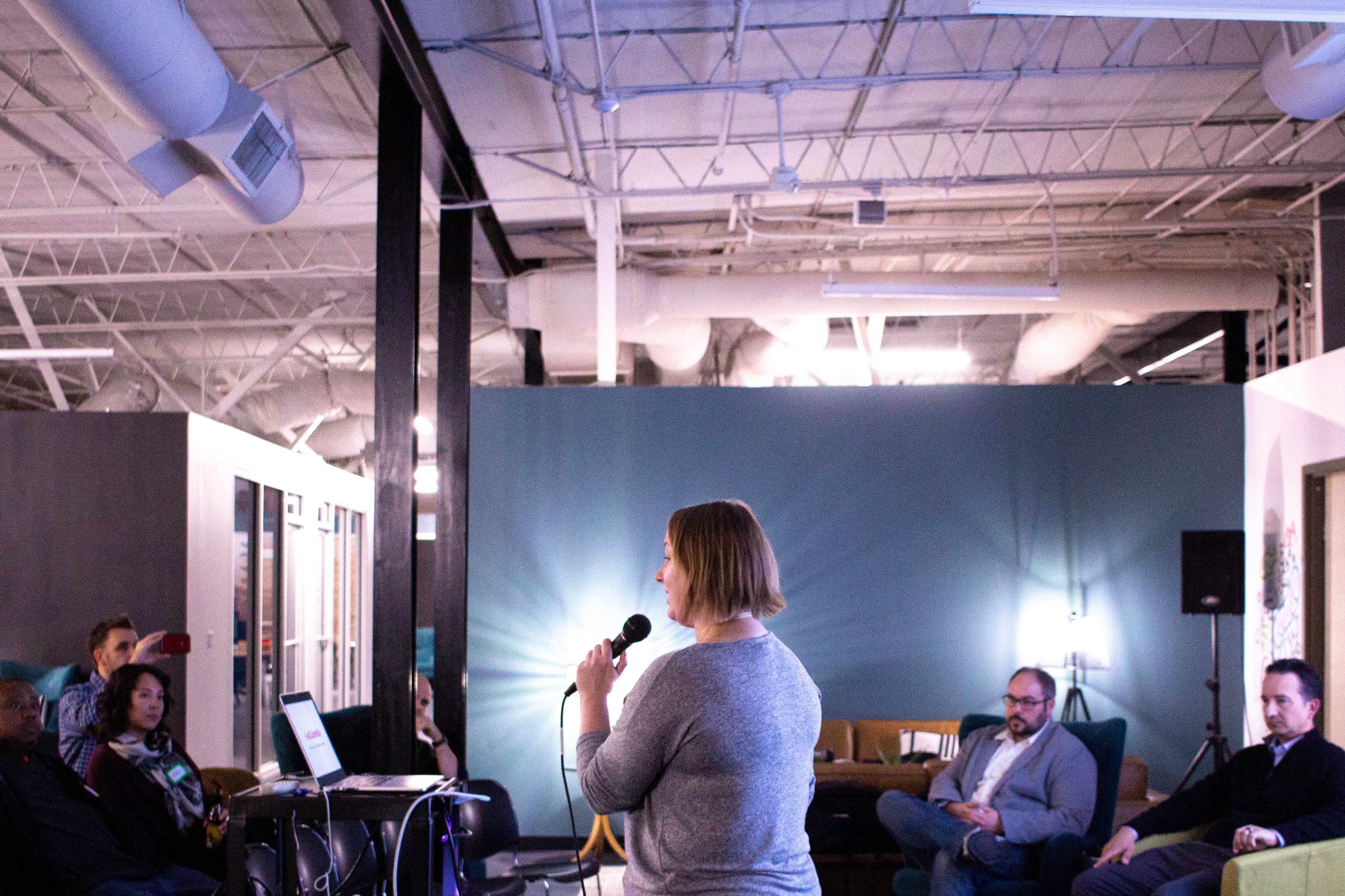 A woman holding a microphone speaks to a small crowd of people.
