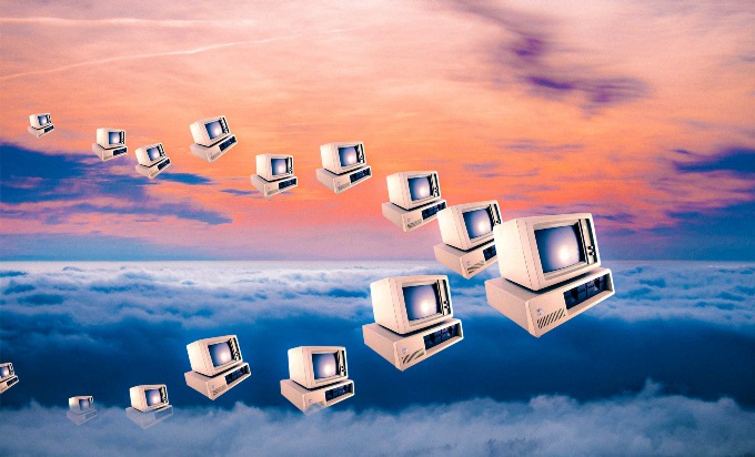 A flock of old PC computers in a V shape fly across a setting sun, mimicking birds.