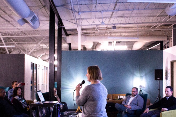A woman holding a microphone speaks to a small crowd of people.