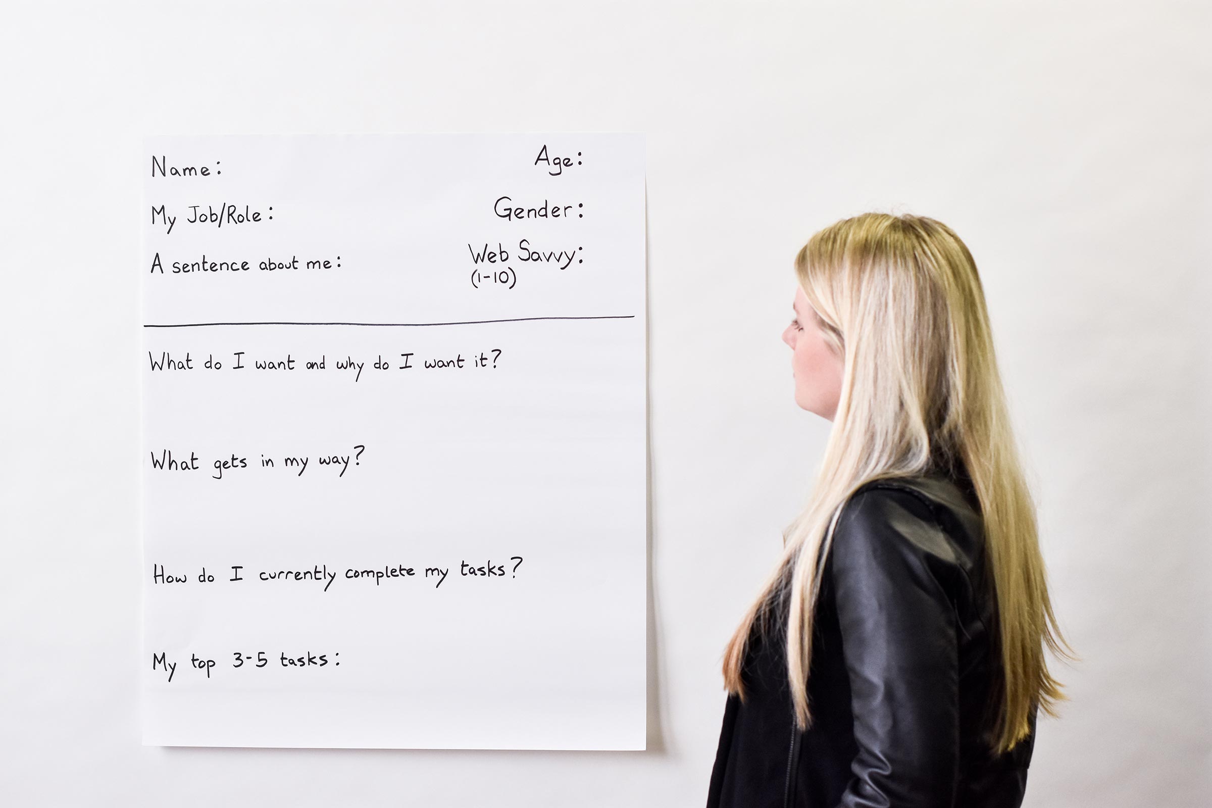 fullcard An image of a woman looking at at persona sheet. On the page, it asks for name, job/role, age, gender, a sentence about them, and to rate how web savvy they are on a scale of 1 to 10. There are four questions that read as follows:
